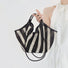 Model holding a Black and white striped polyester and PU leather basket bag handheld , great for everyday.