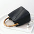 Black textured vegan leather bucket bag with a natural bamboo handle on a minimalist white background.