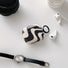Front view of Black and white wavy silicone AirPods case cover with a black keyring, next to white AirPods.