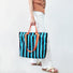 Polyester tote bag with bold blue and black stripes, orange grab handles and shoulder straps.