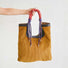A hand holding the Designer Gentle Beam Tote Bag by its unique braided rope handle against a white background.