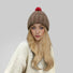 Woman wearing brown knitted pompom beanie with red accent next to a white sweater.