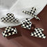 Five black and white checkerboard acrylic hair claws in various sizes and shapes on a brown and white surface.