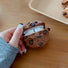 Model Hands holding a brown Chocolate Cookies AirPods case cover, easy to carry for commutes and travel.
