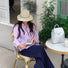 Woman in a lavender striped shirt and navy pants wearing a beige nylon Colorband Flip Bucket Hat with a blue band, reading outdoors.