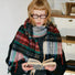 Model wearing soft, fringed Crimson Meadow Plaid Scarf in wool-acrylic blend, featuring red, green, and blue hues.