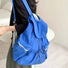 Blue nylon ultralight drawstring backpack with white straps and front zip pockets, worn by a person.