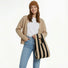 A woman wearing a brown cardigan and jeans holding a black and khaki stripe woven tote bag, showcasing French-chic style.