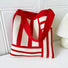 Angled view of Red and white geometric line knitted bag with elastic shoulder strap and open top.