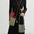 Four hanging ball leather crossbody bags in red, brown, grey and khaki green, worn together by a person.