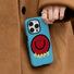 Close-up of model holding blue soft-touch silicone smile case. Playful aesthetic for casual daily outings.
