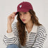 Female model wearing a burgundy cotton baseball cap with white heart embroidery paired with a striped polo.