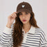 Model wearing a chocolate brown heart embroidered cap paired with a preppy striped polo shirt.