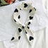 Angled view of White polyester skinny scarf with black heart pattern, tied in a knot in navy, easy for travel packing.