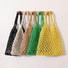 Five cotton rope hollow crochet tote bags in black, white, tan, green, and yellow hanging on a wooden rack.