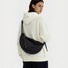 Model wearing a black nylon crescent sling bag over a white hoodie, large hobo bag for everyday carry.