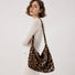 Model wearing the slouchy leopard print hobo tote bag on her shoulder with a white long-sleeve knit.