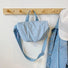 Light blue crinkle crossbody bag hanging on a wooden hook next to a denim jacket.