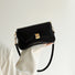 Black PU leather arc baguette shoulder bag with gold hardware, held by a hand.
