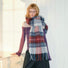 Model wearing Midnight Blaze Plaid Scarf, a long wool blend scarf with red, blue, and white plaid pattern and fringe.