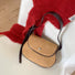 Front view of the khaki mini suede saddle bag on a clean background beside a red sweater.