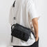 Black and gray plaid waterproof nylon sling bag with adjustable strap, worn crossbody.