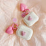 Two white silicone AirPods cases with pink heart charms and smiley face keychains.