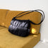 Front view of Black pleated cloud bag with an adjustable strap, resting on a yellow couch Pleated Cloud.