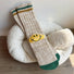 Khaki knit ribbed crew socks with a yellow embroidered smiley face patch.