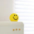 Angled view of Bright yellow polyethylene smiley face piggy bank ornament on a white surface.