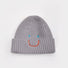 Gray ribbed knit beanie with an embroidered blue-eyed smiley face, adding a playful touch to winter gear.