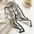 Angled view of White satin skinny scarf with black vertical stripes and border, draped on a beige blazer, easy.