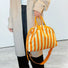 Close-up of model holding orange striped bag by the grab handle; highlighting the drawstring closure and PU leather detail.