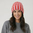 Model wearing Striped Fluffy Knit Beanie in pink. Soft, lightweight construction with a trendy striped design.