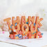 Close-up of greeting card with colorful floral design and 3D Thank You Text.