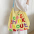 Model carrying a yellow Think About Earth Tote Bag on her shoulder, easy for commuting and weekends.