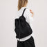 Model wearing the classic black 2-way drawstring backpack over one shoulder as a tote.