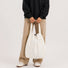 Model holding the off-white 2-way convertible tote bag by its shoulder handles.