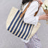 Model carrying a Vertical striped straw tote bag with blue and natural stripes on her shoulder.