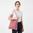 Model styling a purple and orange argyle pleated knit bag for a vibrant look.