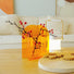 Modern orange acrylic vase with red berry branches and a portable white lantern on a wooden coffee table.