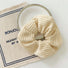 Front view of Cream knitted scrunchie with ribbed texture, resting on a white plate and beige fabric.