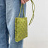 Lime green PU leather woven crossbody bag with a slim strap, held by a person in jeans.