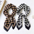 Two satin checkerboard square scarves, one black and white, one black and caramel, tied neatly.