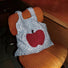 Close-up of Blue and white knit polyester bag with a large red apple design and two grab straps .
