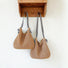 Two straw bags with  different straps lengths hang on the wall: one features a shoulder strap, while the other has a crossbody strap.