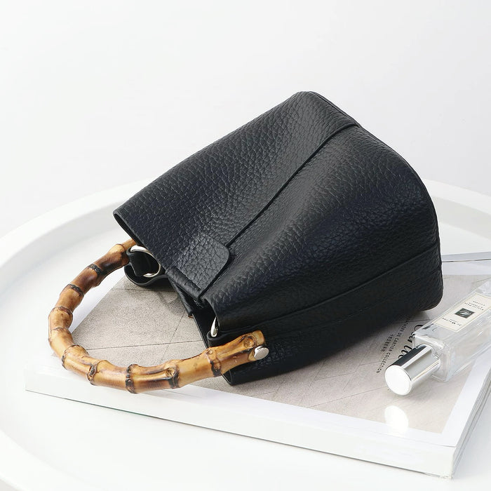 Black textured vegan leather bucket bag with a natural bamboo handle on a minimalist white background.