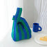 A blue and green vertical stripe knit tote bag placed on a table with a blue mug, perfect for aesthetic lifestyle photography.