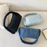 Close-up of Three braided handle denim handbags in dark blue, light blue, and black on a white couch.