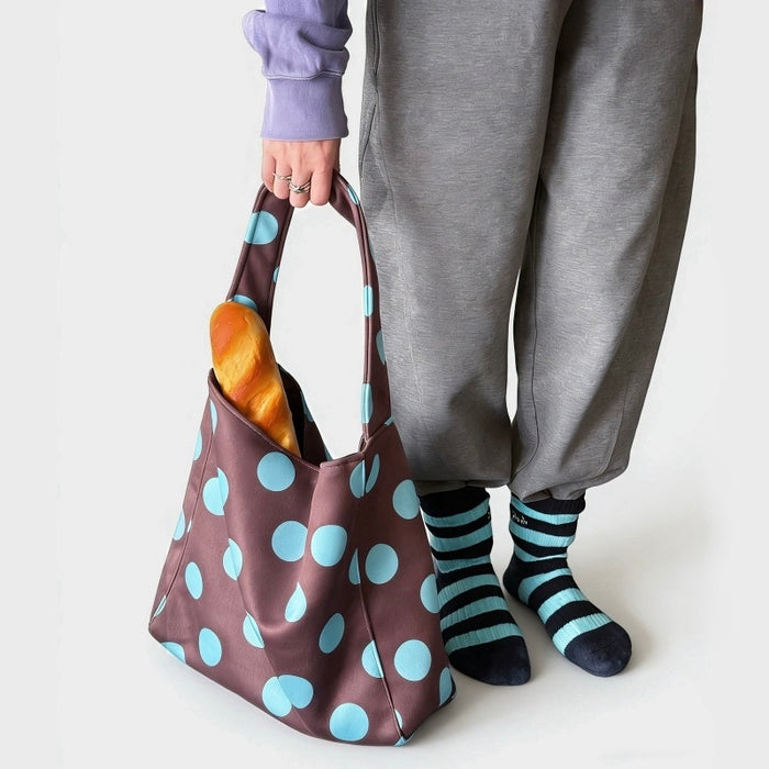 Model holding a brown vegan suede hobo bag with blue polka dots and a soft velvety finish.